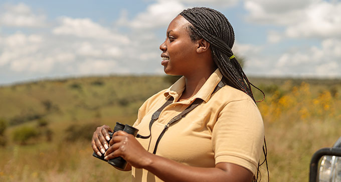 a tour guide holding binoculars and looking to the left into a grassy savannah